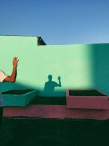 shadow of a man waving, on a minty green building with blue sky behind